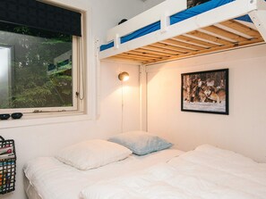 A room with a bunk bed, a single bed, a window with a view of trees, a wall-mounted light, and a framed picture.