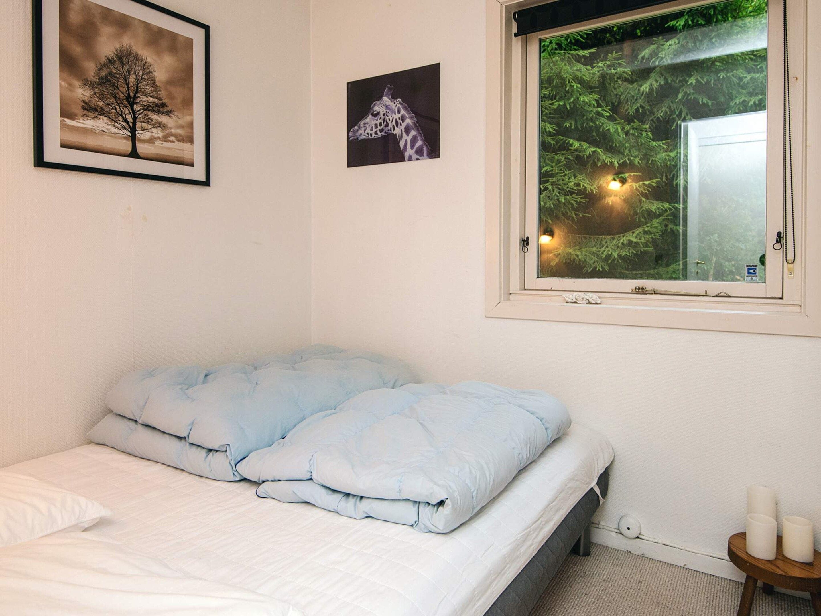 A bedroom with a bed, a window with a view of trees, and two framed pictures on the wall.