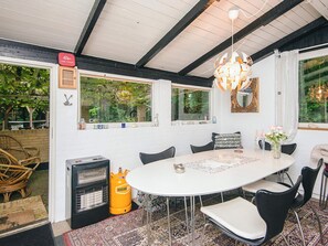A dining area with a round table, chairs, a decorative rug, a heater, and a large window with a view of greenery. - 4 Person Holiday Home in Ans By (Ans)