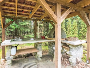 A rustic outdoor kitchen with a stone sink, a red kettle, and a basket of pinecones. - 4 Person Holiday Home in Ans By (Ans)