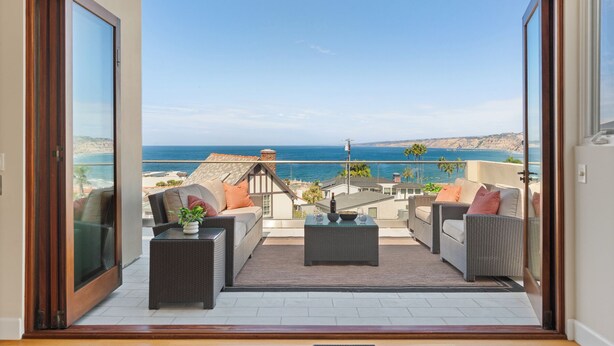 Un balcon agrémenté de meubles en osier, d’une petite table et offrant une vue sur l’océan et les falaises.