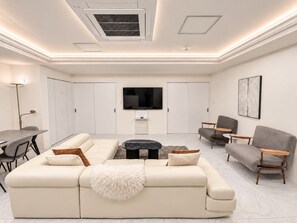 A modern living room with a sectional sofa, a coffee table, and a flat-screen TV mounted on the wall.