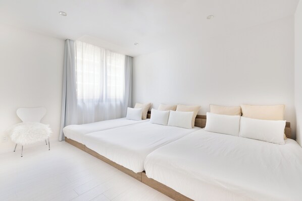 A modern bedroom with a large bed, a fluffy chair, and a window with curtains.