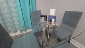 Una mesa con cubierta de vidrio, dos sillas grises, un tarro de vidrio, un objeto negro, un objeto blanco y una tarjeta de agradecimiento.