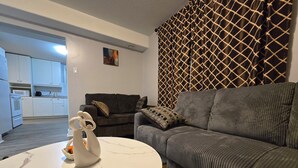 Una sala de estar moderna con un sofá gris, una mesa de centro de mármol blanco y una cocina al fondo.