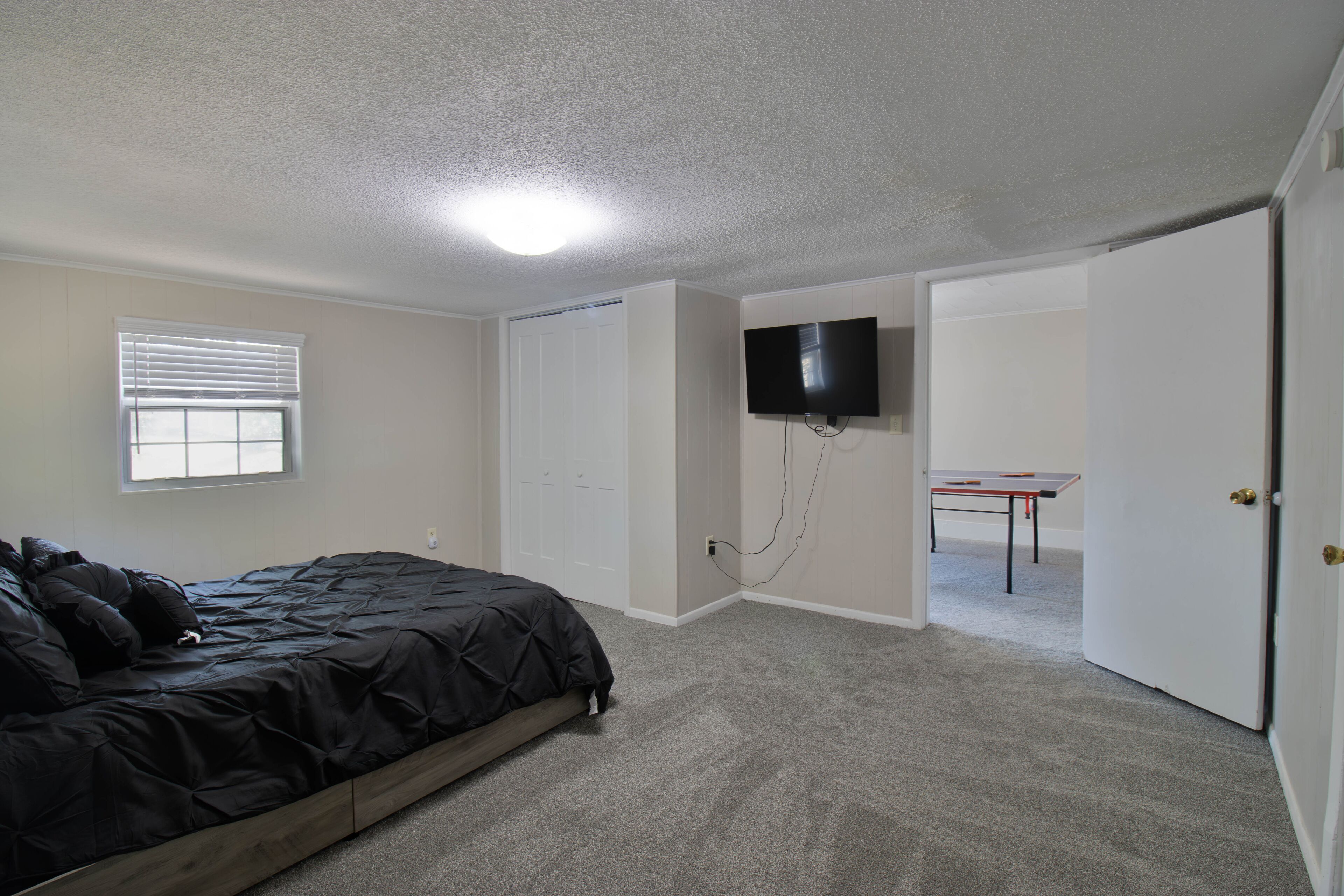 A bedroom with a bed, a television mounted on the wall, and a door leading to another room.