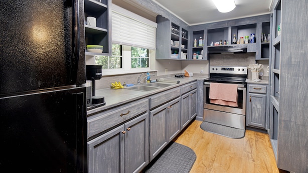 A modern kitchen with grey cabinets, a black refrigerator, stainless steel appliances, and a window with blinds.