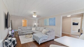 A living room with a grey sectional sofa, a white coffee table, and a white dining table.