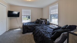 A bedroom with two beds, a television, and large windows with blinds.