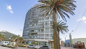 A modern building with a curved facade, multiple floors, and a palm tree in the foreground. - Oceana Suites Lafayette (Punta del Este)
