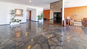 A spacious lobby with a polished stone floor, a reception desk, and a seating area with chairs. - Oceana Suites Lafayette (Punta del Este)