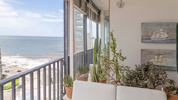 A balcony with a view of the ocean, potted plants, and artwork on the wall. - Oceana Suites Lafayette (Punta del Este)