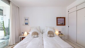 A double bed with white bedding, two bedside tables with lamps, a window with curtains, and a wall-mounted picture frame. - Oceana Suites Lafayette (Punta del Este)