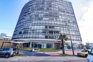 A modern multi-story building with a curved facade, large windows, and a sign indicating a business center. - Oceana Suites Lafayette (Punta del Este)