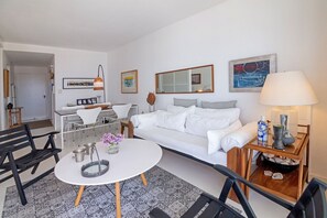 A modern living room with a white sofa, a round coffee table, and a dining area with a white table and chairs. - Oceana Suites Lafayette (Punta del Este)