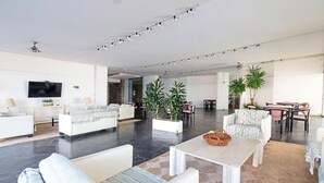 A spacious living area with a flat-screen TV, white sofas, a coffee table, and potted plants. - Oceana Suites Lafayette (Punta del Este)