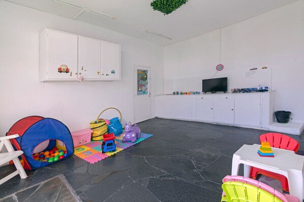 Una sala de juegos con una tienda de campaña, piscina de pelotas y un televisor sobre un mueble.