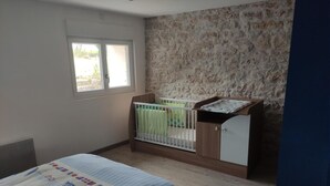 A bedroom with a crib, a window, a stone wall, and a bed with a patterned bedspread. - House near the train station with outdoor space (Neufchâteau)