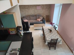 Un espacio habitable compacto con kitchenette, un conjunto de sofás, una mesa de comedor y una ventana pequeña con una planta de orquídea.