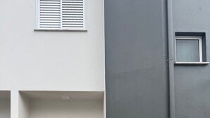 A building with two wooden doors, a small window, and a grey wall. - Beach house in a gated community. Enclosed area with barbecue | Small pets allowed (Caraguatatuba)