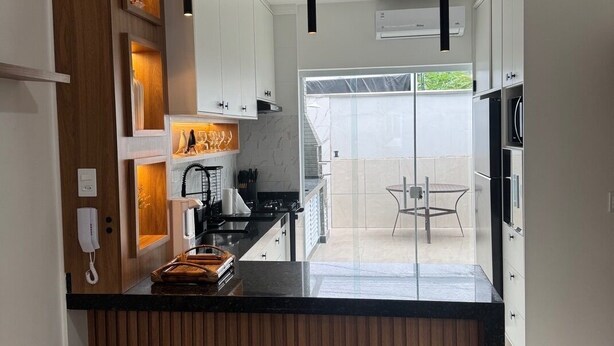 A modern kitchen with a central island, wooden accents, and pendant lighting. - Beach house in a gated community. Enclosed area with barbecue | Small pets allowed (Caraguatatuba)