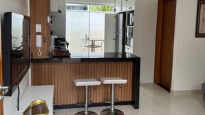 A modern kitchen with a central island, two bar stools, a built-in refrigerator, and a hanging light fixture. - Beach house in a gated community. Enclosed area with barbecue | Small pets allowed (Caraguatatuba)