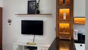 A modern kitchen with a black countertop, white cabinetry, and a built-in TV. - Beach house in a gated community. Enclosed area with barbecue | Small pets allowed (Caraguatatuba)