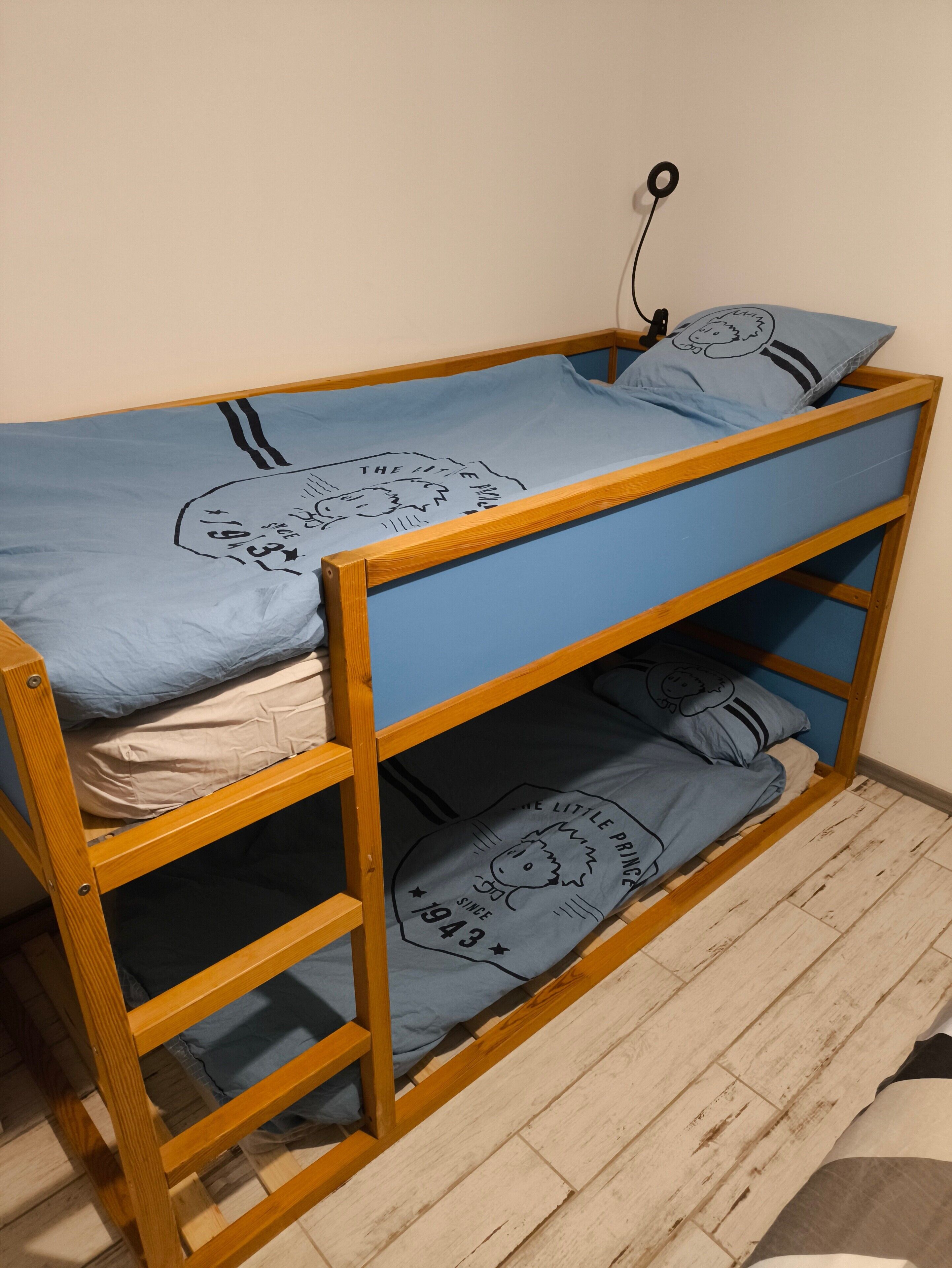 A bunk bed with a blue mattress and pillows, a wooden frame, and a wall-mounted electrical outlet.