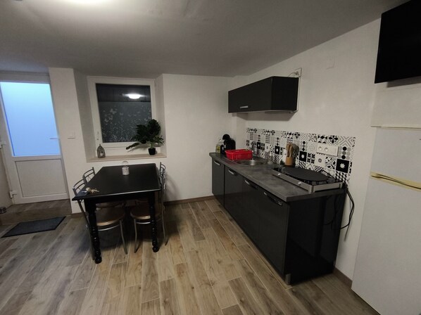A compact kitchen with a dining table, chairs, a window, a potted plant, and a tiled backsplash.