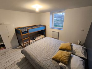A bedroom with a bunk bed, a window, a radiator, and a wardrobe.