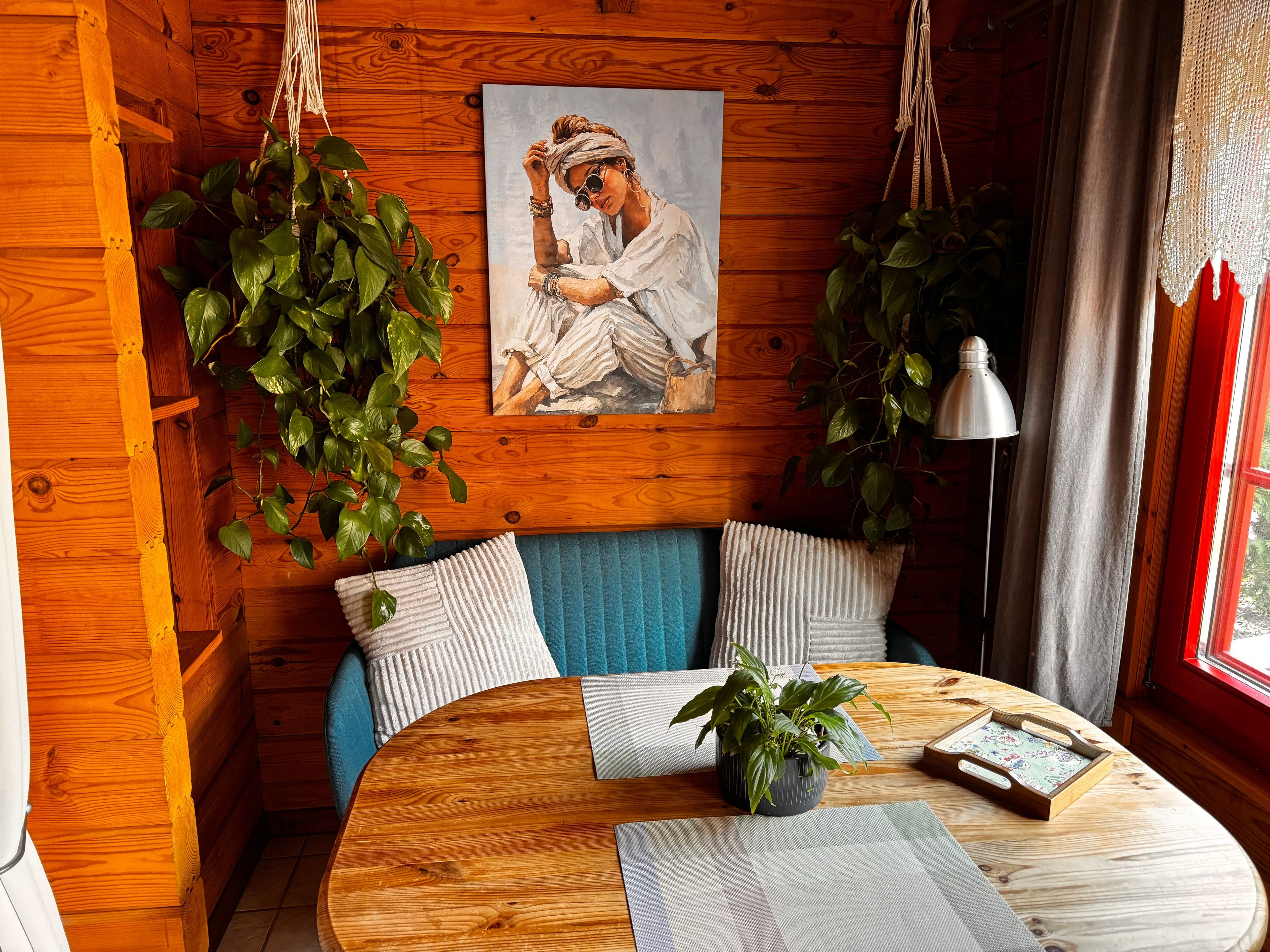 Ein gemütliches Zimmer mit Holzwänden, einem runden Holztisch, einem blauen Sofa und hängenden Pflanzen.