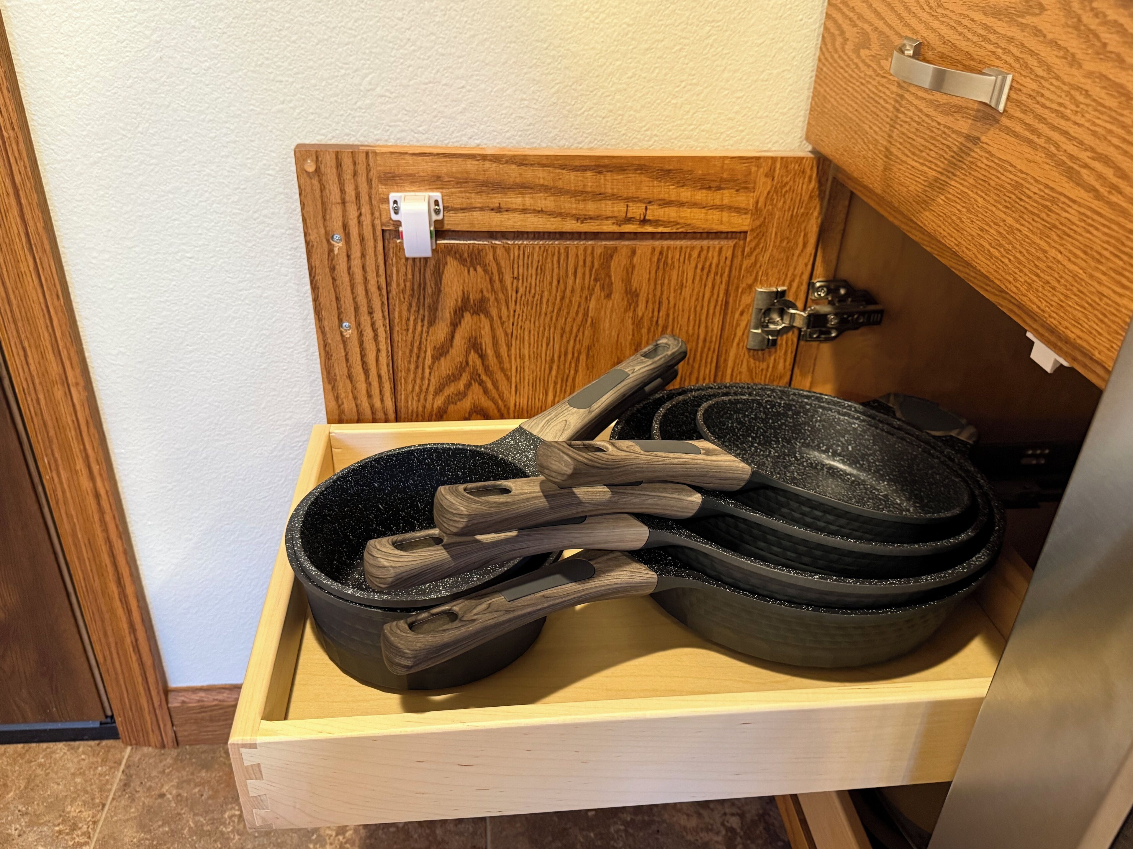 A wooden cabinet with a drawer containing a black frying pan and wooden-handled utensils.