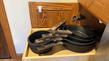 A wooden cabinet with a drawer containing a black frying pan and wooden-handled utensils.