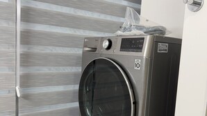 Ein kompakter, moderner Waschraum mit einer Waschmaschine und einem Trockner mit Frontlader, einem Fenster mit horizontalen Jalousien und einer kleinen Plastiktüte auf dem Trockner.