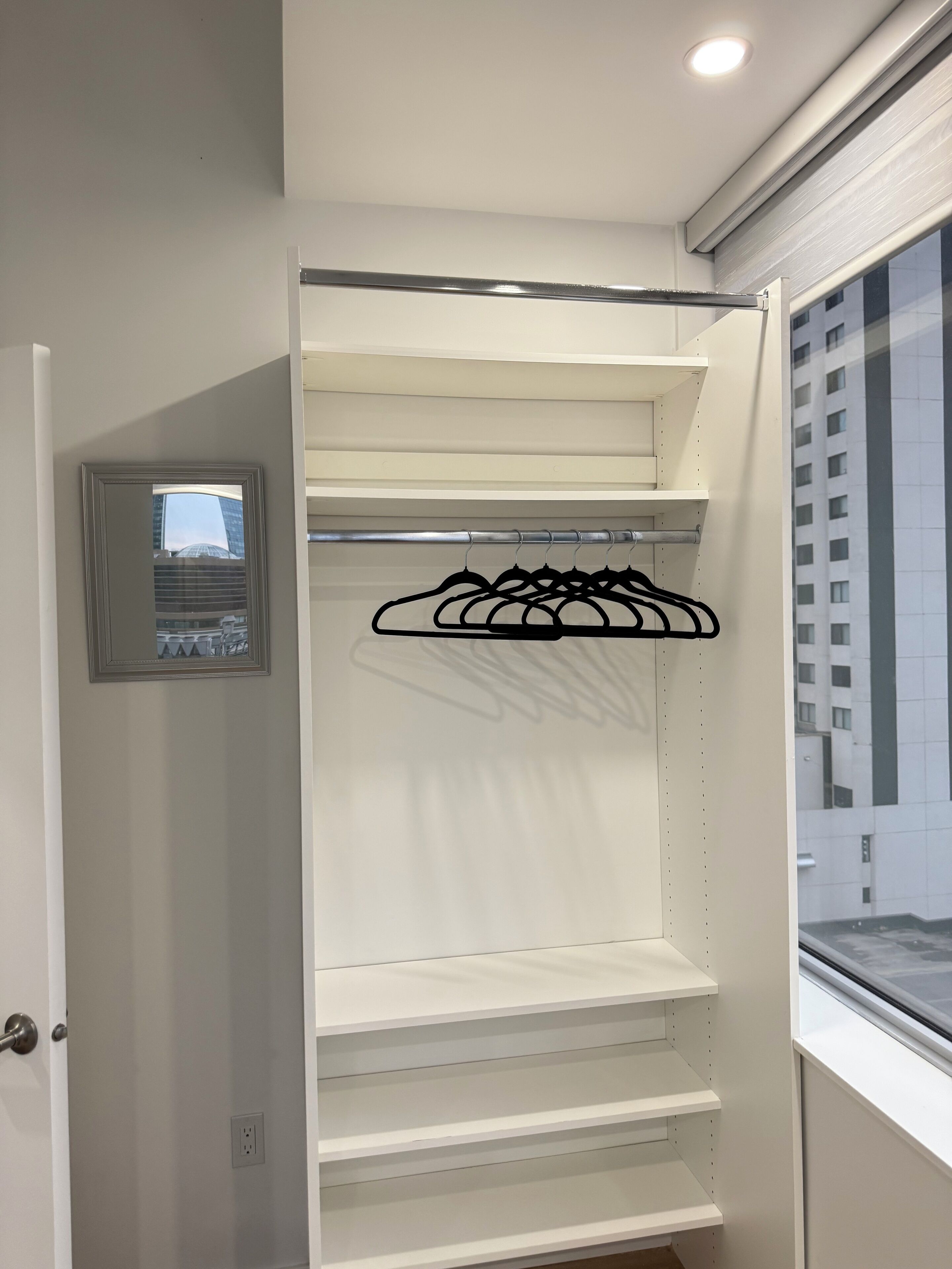 A walk-in closet with open shelves and a black hanger rack.