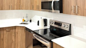 Eine moderne Küche mit Holzausstattung, einer Edelstahl-Mikrowelle, einem schwarzen Backofen und einem Geschirrspüler.
