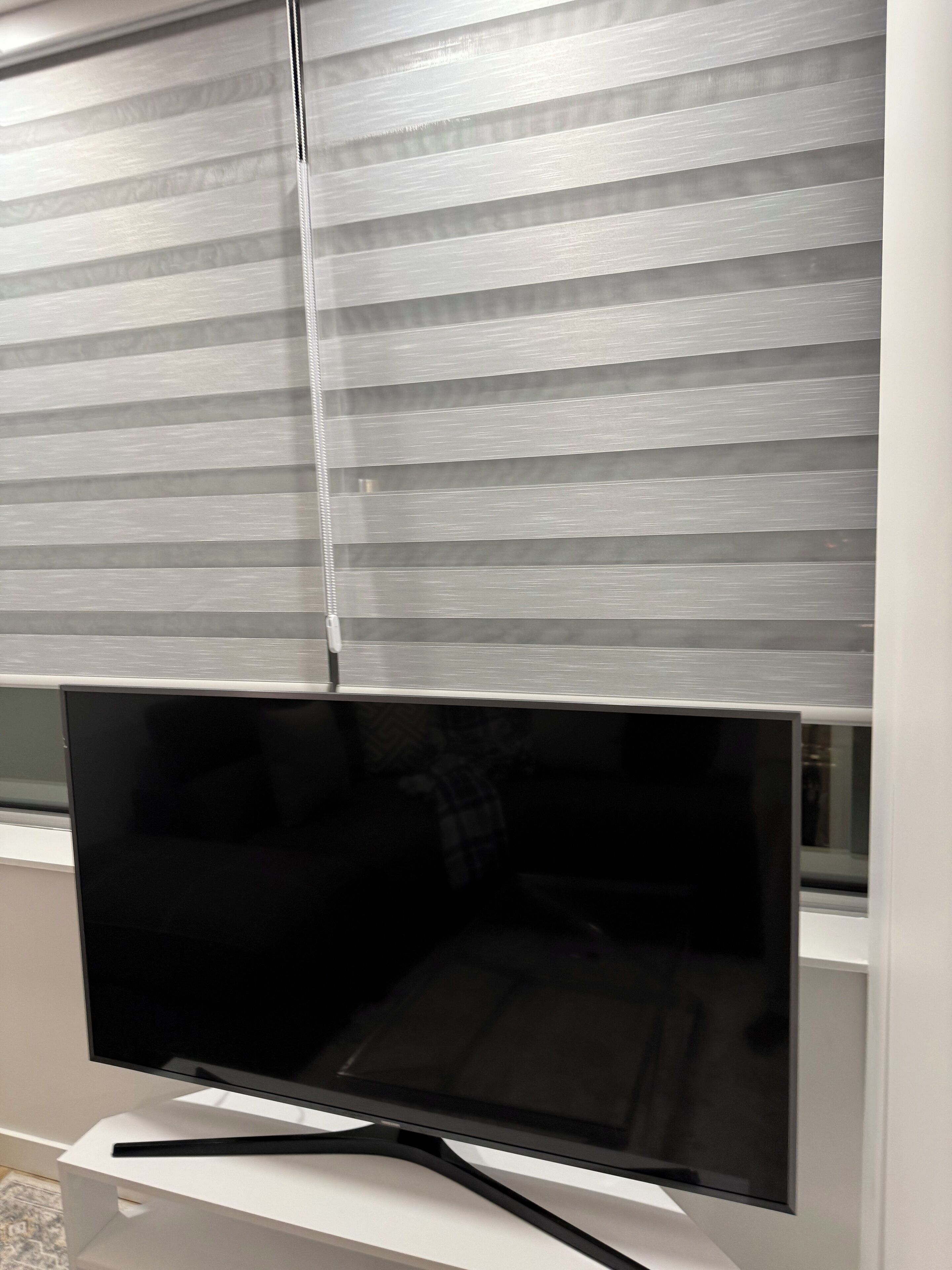 Un téléviseur à écran plat, fixé sur un support blanc, avec une télécommande noire.