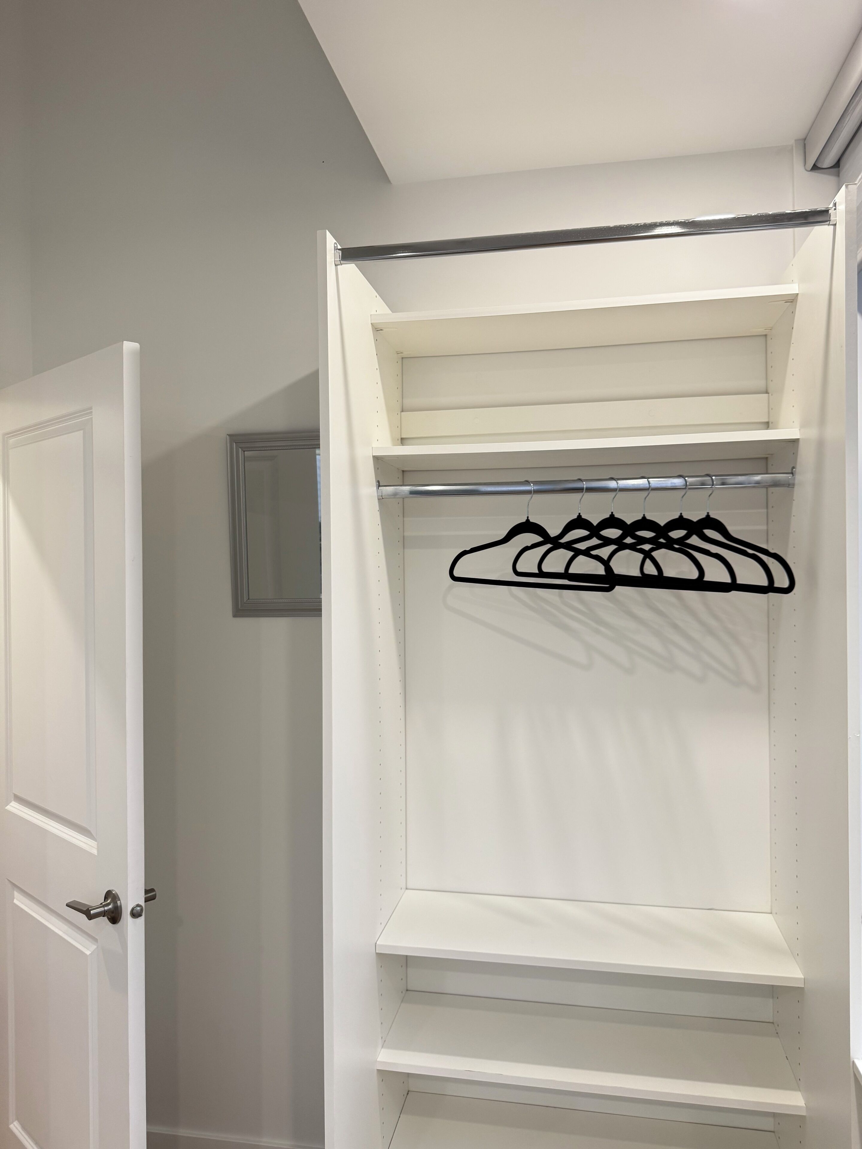 Un dressing blanc avec des portes ouvertes, muni d’une tringle en métal et de cintres noirs.
