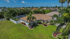 A residential house with a tiled roof, surrounded by lush greenery and palm trees. - Relaxing outdoor with pool and hot tub! (Cape Coral)