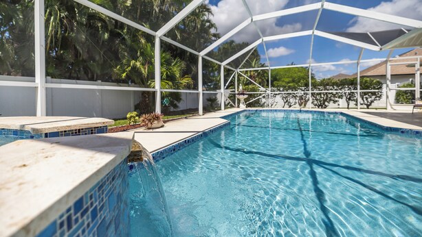 A swimming pool with a white roof and blue tiles, surrounded by palm trees and a clear sky. - Relaxing outdoor with pool and hot tub! (Cape Coral)