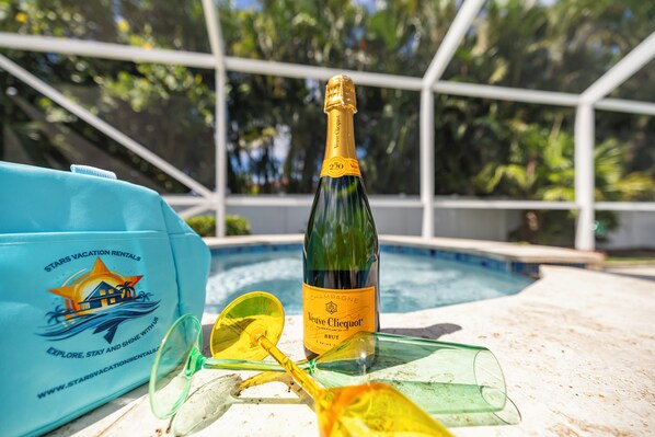 A bottle of Veuve Clicquot Brut champagne, a pair of sunglasses, and a blue bag with a logo and text on a poolside setting.