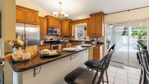 A kitchen with wooden cabinets, a stainless steel refrigerator, a microwave, and a coffee maker. There is a dining area with a table and chairs. - Relaxing outdoor with pool and hot tub! (Cape Coral)