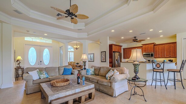 A spacious living room with a large sectional sofa, a coffee table, and a dining area with a chandelier. - Southern Exposure - 4bed/3bath - Sands Area - Stars Vacation Rentals (Cape Coral)