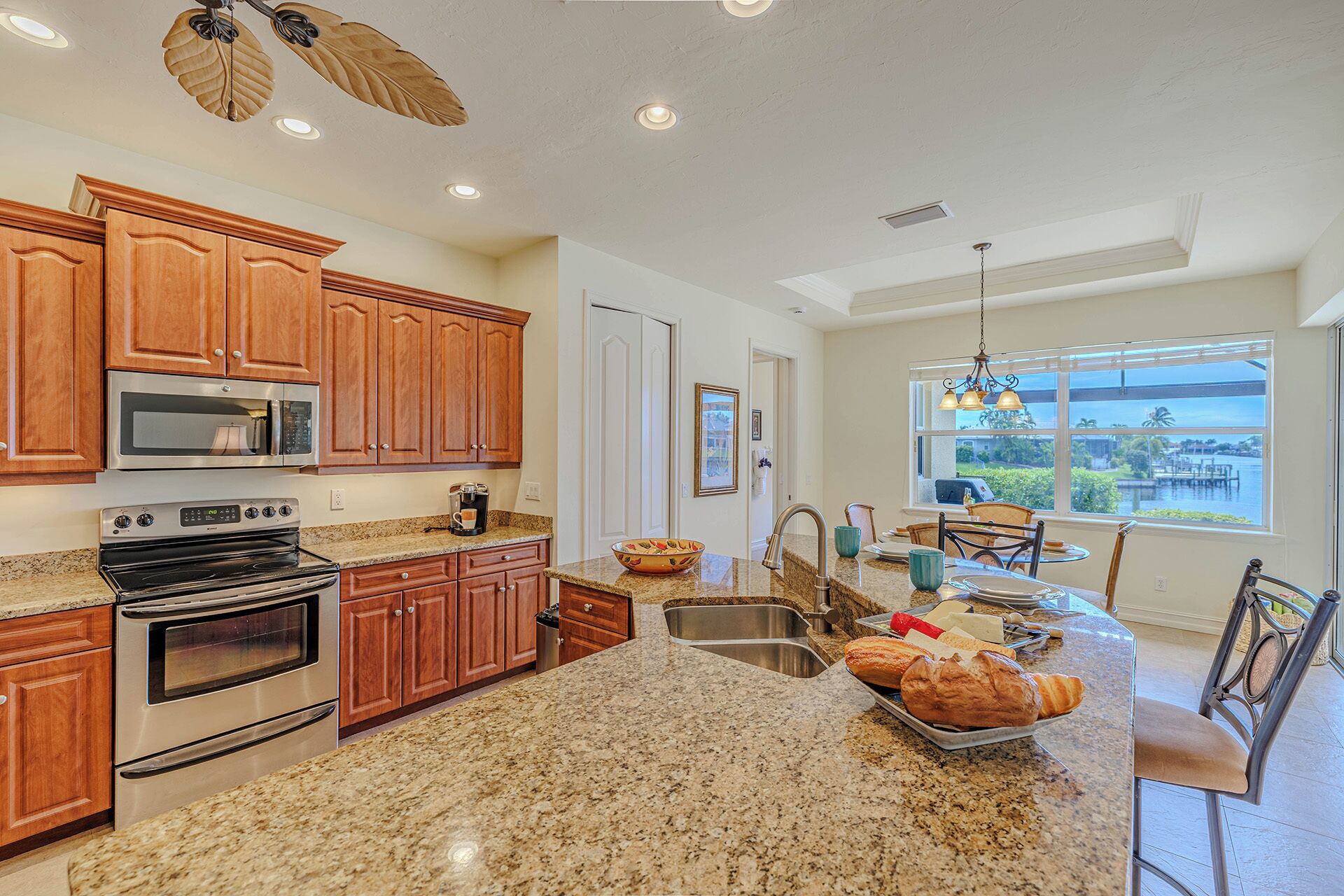 A kitchen with granite countertops, stainless steel appliances, wooden cabinets, and a view of the outdoors through large windows.