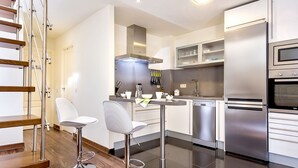 Una cocina moderna con electrodomésticos de acero inoxidable, una barra con taburetes y una escalera de madera.