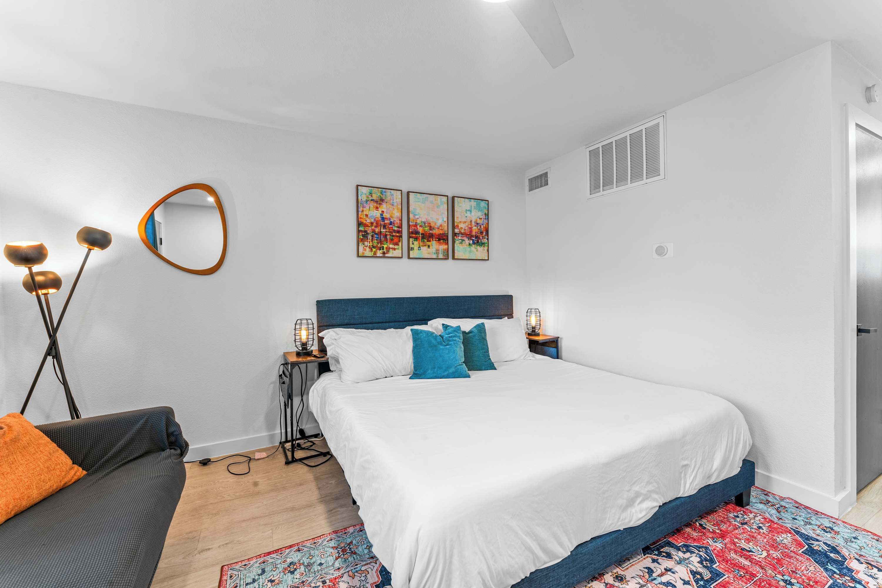 A modern bedroom with a large bed, a sofa, a floor lamp, and artwork on the wall.