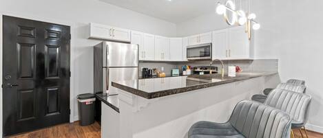 A modern kitchen with white cabinets, stainless steel appliances, and a central island with bar stools.