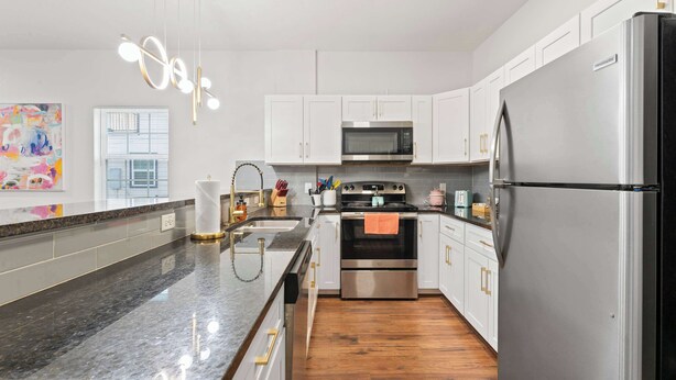 A modern kitchen with white cabinets, stainless steel appliances, a granite countertop, and a wooden floor. - NRG Medcenter 2BD 2 5BA w Fencedyard Washerdryer (Houston)