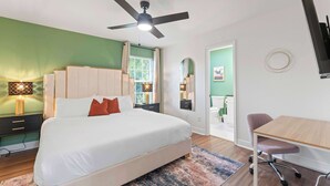Une chambre à coucher comprenant un lit, un bureau, une chaise, un ventilateur de plafond et une fenêtre.