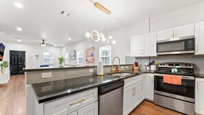 Une cuisine moderne avec des meubles blancs, un plan de travail noir, des appareils en acier inoxydable et un plancher en bois.